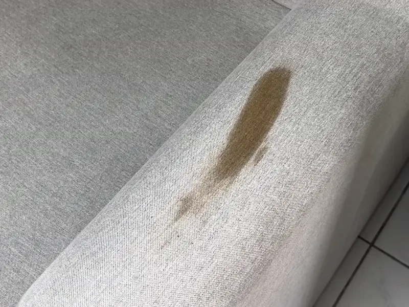 Accoudoir d'un canapé en tissu gris clair taché, avant nettoyage